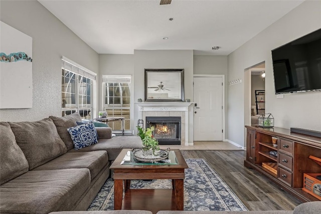 living room with a tiled fireplace, dark wood-type flooring, and ceiling fan