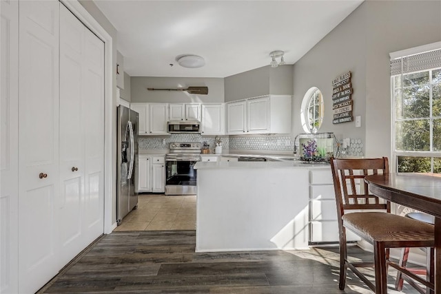 kitchen with backsplash, stainless steel appliances, kitchen peninsula, and white cabinets