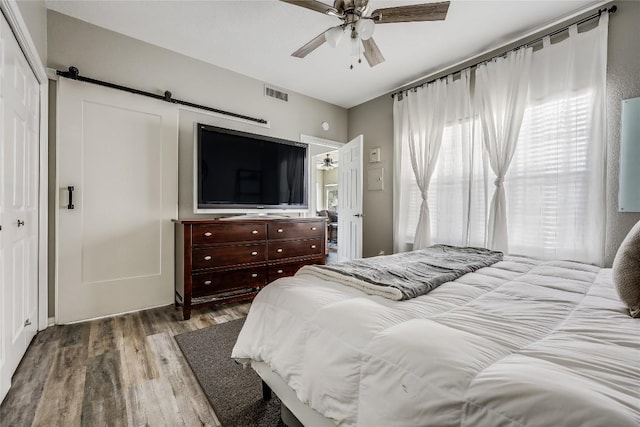 bedroom featuring wood-type flooring, a barn door, ceiling fan, and a closet