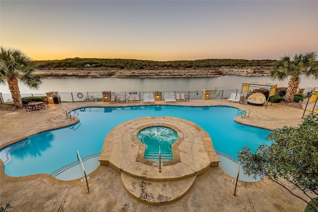 pool at dusk with a patio area, a hot tub, and a water view