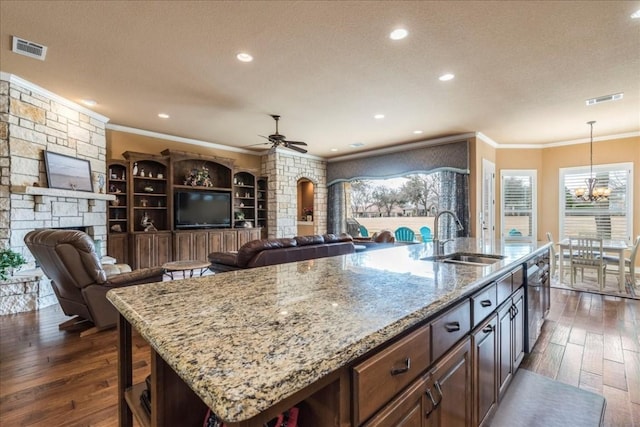 kitchen featuring sink, hanging light fixtures, ornamental molding, a kitchen island with sink, and light stone countertops