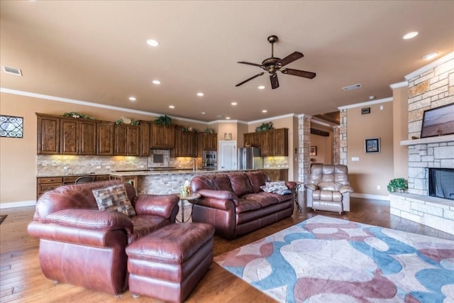 living room with a stone fireplace, sink, light hardwood / wood-style flooring, ornamental molding, and ceiling fan