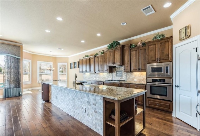 kitchen with dark wood-type flooring, tasteful backsplash, hanging light fixtures, a center island with sink, and stainless steel appliances