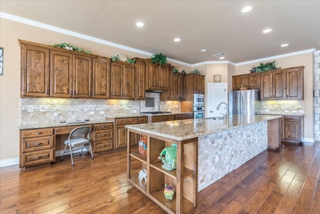 kitchen with appliances with stainless steel finishes, sink, light stone counters, dark wood-type flooring, and a center island with sink