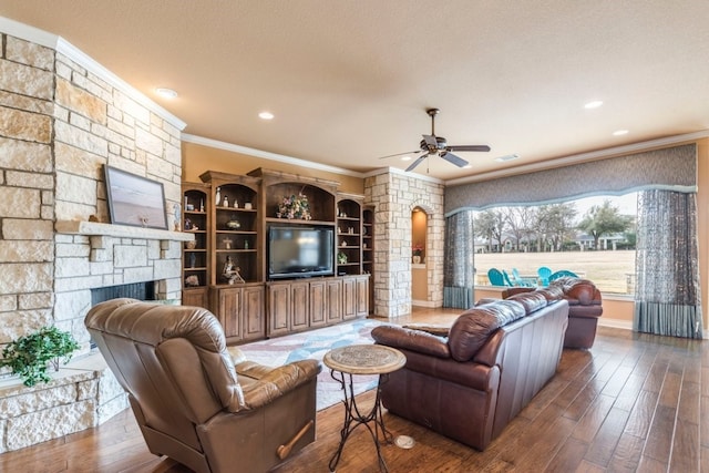 living room with ornamental molding, a stone fireplace, dark wood-type flooring, and ceiling fan