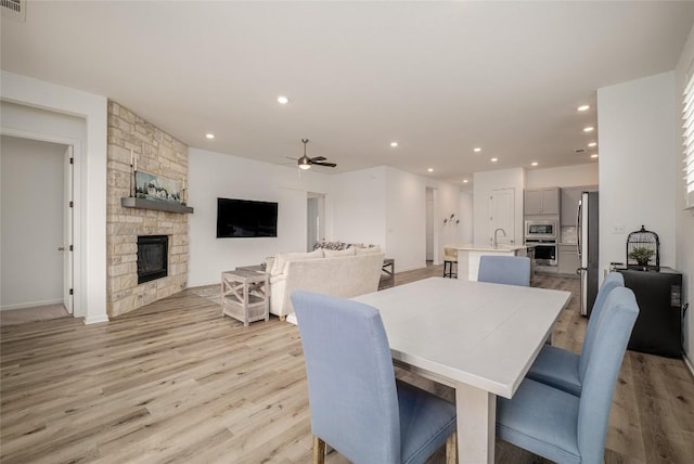 dining area featuring sink, light hardwood / wood-style flooring, a fireplace, and ceiling fan