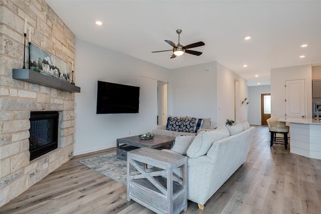 living room featuring a stone fireplace, ceiling fan, and light wood-type flooring