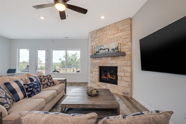 living room with hardwood / wood-style flooring, ceiling fan, and a stone fireplace