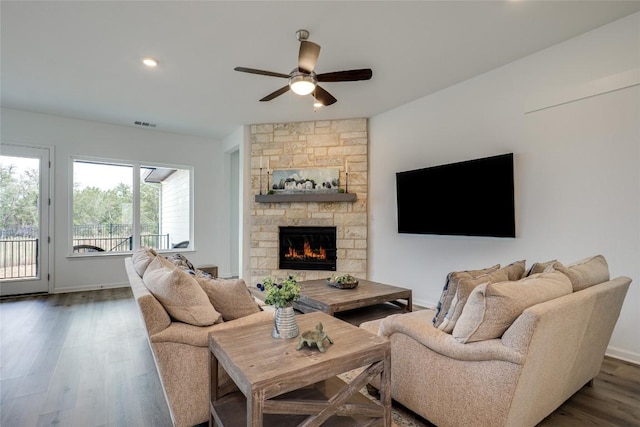 living room featuring a stone fireplace, dark wood-type flooring, and ceiling fan