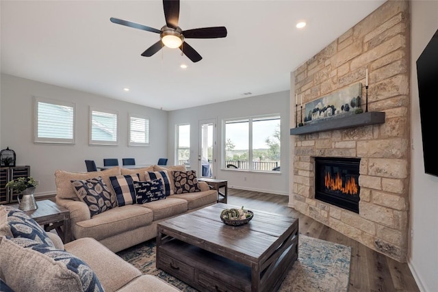 living room featuring a stone fireplace, dark hardwood / wood-style floors, and ceiling fan