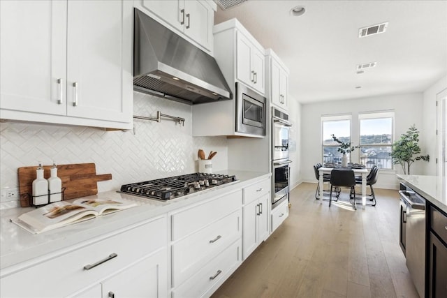 kitchen with white cabinetry, tasteful backsplash, light hardwood / wood-style flooring, appliances with stainless steel finishes, and light stone countertops