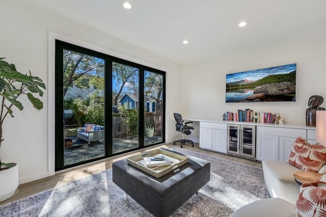 living room with wine cooler, built in desk, and light wood-type flooring