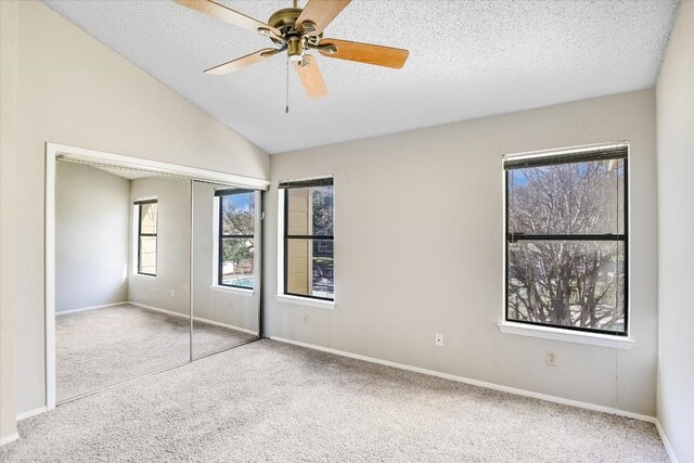 unfurnished bedroom featuring lofted ceiling, light colored carpet, ceiling fan, a textured ceiling, and a closet