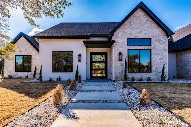 view of front facade featuring a shingled roof, stone siding, and stucco siding