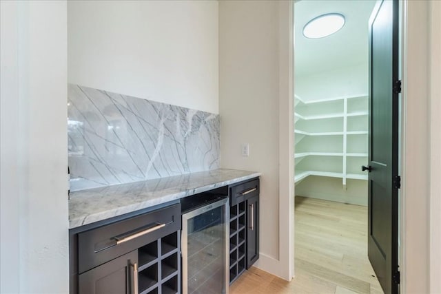 bar featuring tasteful backsplash, a bar, light wood finished floors, and beverage cooler