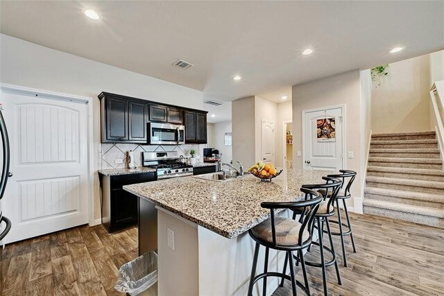 kitchen with a breakfast bar, sink, an island with sink, stainless steel appliances, and hardwood / wood-style floors