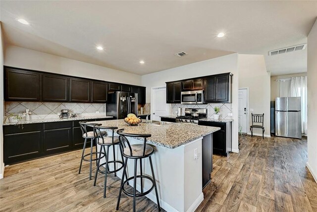 kitchen with stainless steel appliances, an island with sink, sink, and light hardwood / wood-style floors