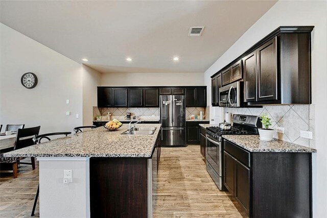 kitchen featuring stainless steel appliances, a kitchen island with sink, sink, and light hardwood / wood-style flooring