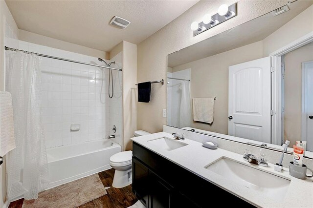 full bathroom with hardwood / wood-style flooring, vanity, toilet, a textured ceiling, and shower / bath combo with shower curtain