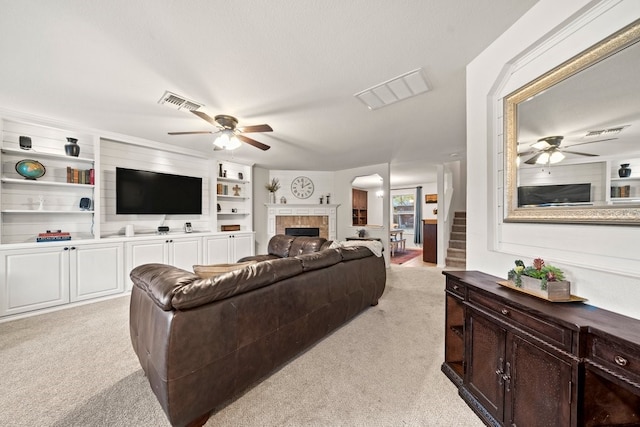 carpeted living room with built in shelves, ceiling fan, and a tiled fireplace