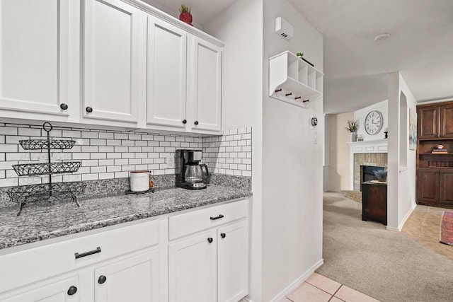 kitchen featuring light carpet, backsplash, light stone counters, and white cabinets