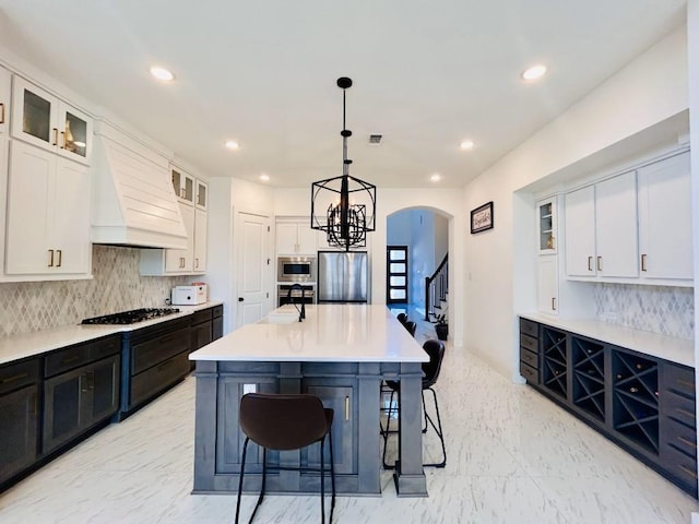 kitchen with appliances with stainless steel finishes, hanging light fixtures, an island with sink, white cabinets, and custom exhaust hood