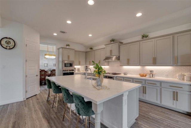 kitchen with a breakfast bar, gray cabinetry, tasteful backsplash, an island with sink, and stainless steel appliances