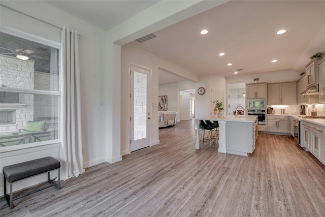 kitchen featuring a breakfast bar area, stainless steel appliances, a center island with sink, a stone fireplace, and light wood-type flooring