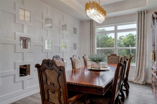 dining space with a raised ceiling, crown molding, a notable chandelier, and light hardwood / wood-style flooring