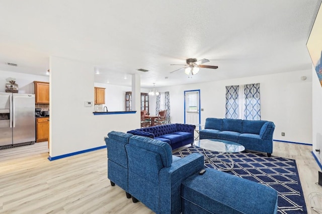 living room featuring ceiling fan with notable chandelier and light wood-type flooring