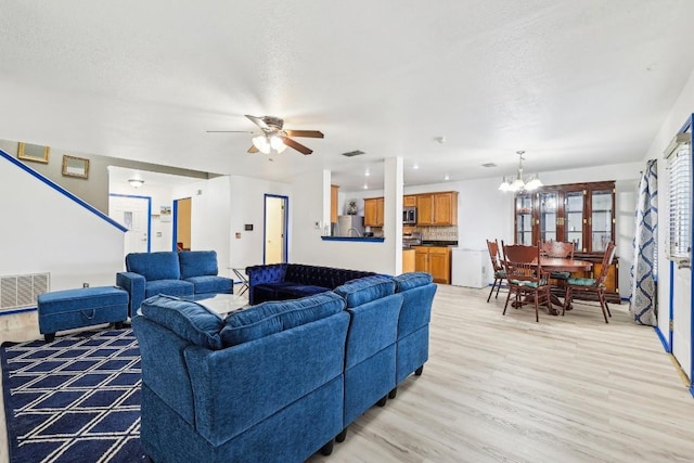 living room featuring ceiling fan with notable chandelier, a textured ceiling, and light hardwood / wood-style flooring