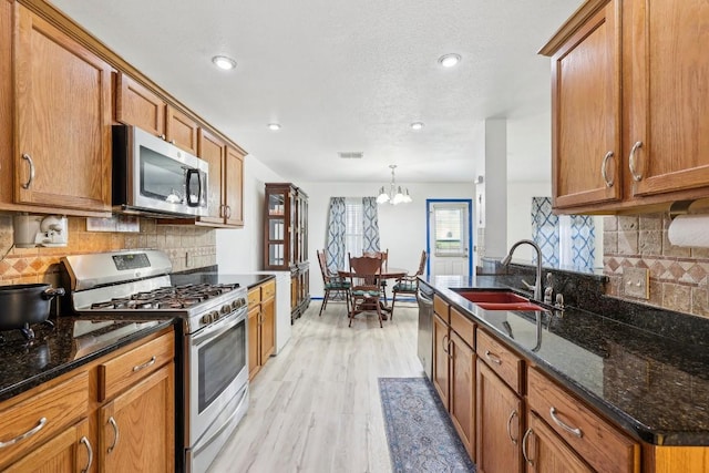 kitchen with sink, appliances with stainless steel finishes, hanging light fixtures, dark stone counters, and a chandelier