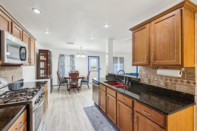 kitchen with sink, stainless steel appliances, light hardwood / wood-style floors, decorative light fixtures, and dark stone counters