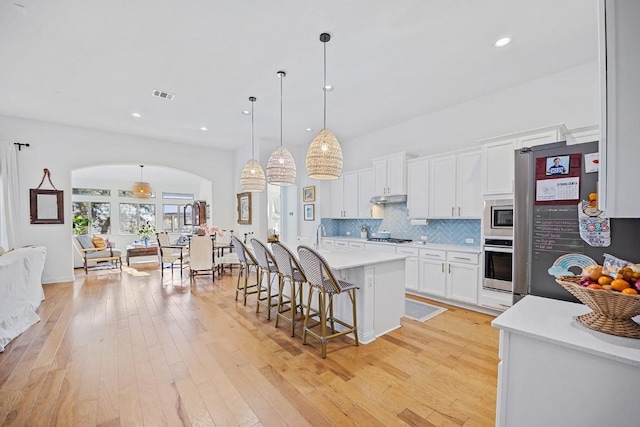 kitchen with white cabinetry, hanging light fixtures, stainless steel appliances, tasteful backsplash, and a center island with sink