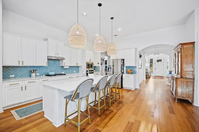 kitchen with appliances with stainless steel finishes, an island with sink, white cabinets, a kitchen breakfast bar, and hanging light fixtures