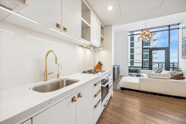 kitchen with sink, dark wood-type flooring, white cabinetry, decorative light fixtures, and oven