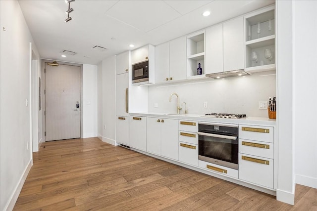 kitchen with sink, appliances with stainless steel finishes, white cabinets, light hardwood / wood-style floors, and exhaust hood