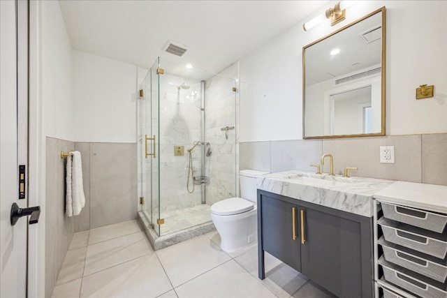 bathroom with tile patterned floors, toilet, tile walls, vanity, and a shower with door