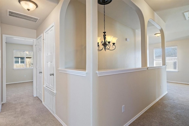 hall with light carpet and an inviting chandelier