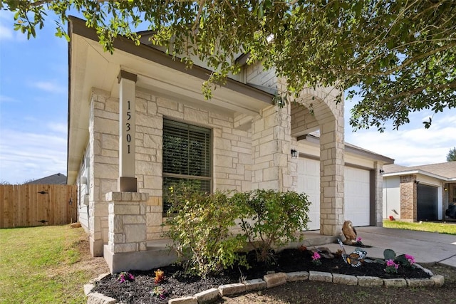 exterior space with an attached garage, stone siding, fence, and concrete driveway