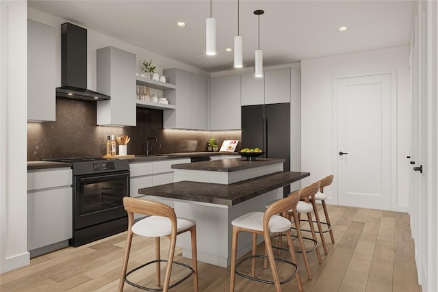 kitchen featuring a kitchen island, a kitchen bar, wall chimney exhaust hood, black appliances, and light hardwood / wood-style flooring