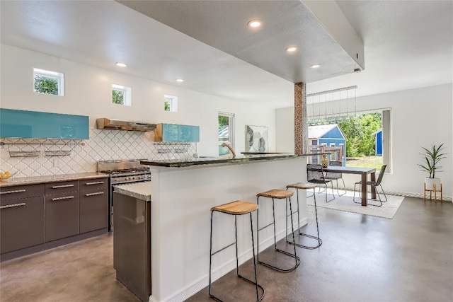 kitchen featuring a breakfast bar area, stainless steel range with gas stovetop, a center island with sink, and backsplash