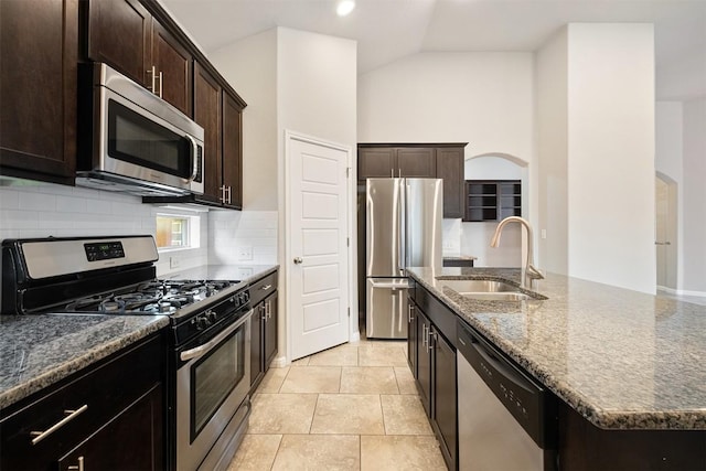 kitchen with sink, vaulted ceiling, dark stone countertops, an island with sink, and stainless steel appliances