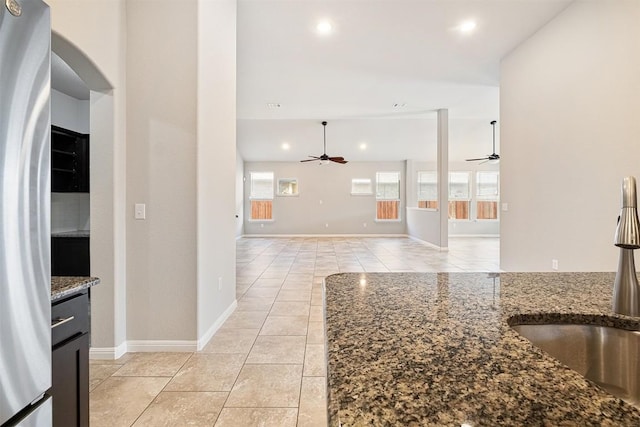 kitchen featuring stainless steel fridge, dark stone counters, and ceiling fan