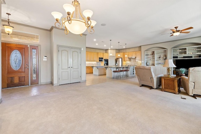 carpeted living room featuring crown molding, ceiling fan with notable chandelier, and built in shelves