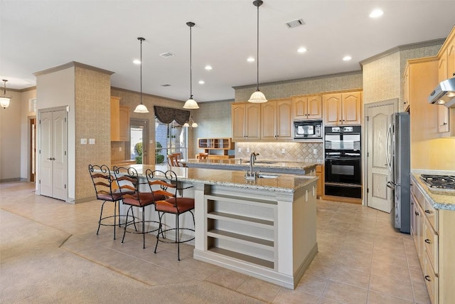 kitchen with light stone counters, appliances with stainless steel finishes, decorative light fixtures, and a center island with sink