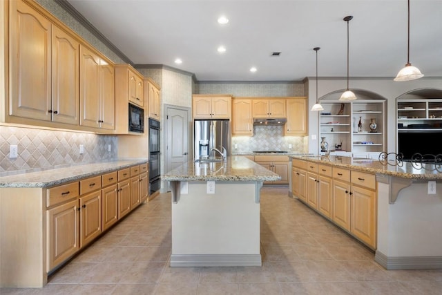 kitchen featuring decorative light fixtures, light stone countertops, a center island with sink, and black appliances