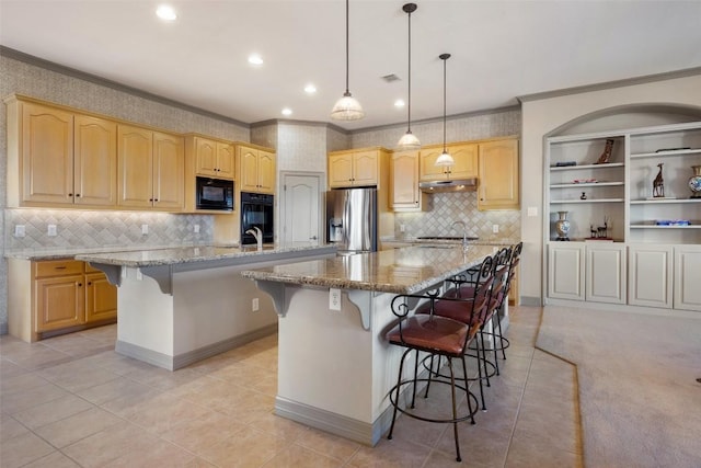 kitchen with a breakfast bar, light stone counters, hanging light fixtures, an island with sink, and black appliances