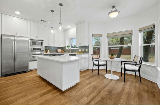 kitchen with light hardwood / wood-style flooring, white cabinetry, hanging light fixtures, backsplash, and built in appliances