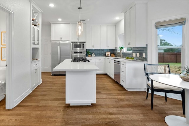 kitchen with white cabinetry, appliances with stainless steel finishes, decorative light fixtures, and a center island